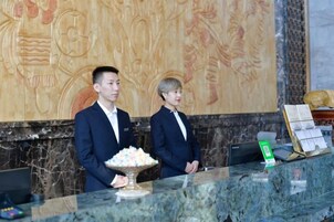 Dos personas de pie en la recepción, frente a un mostrador de mármol, un mural decorativo y un bol de aperitivos.