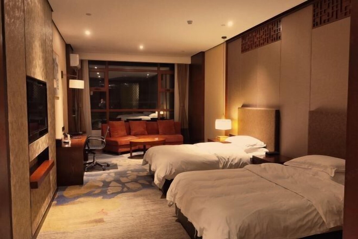 Een hotelkamer met twee bedden, een sofa, een bureau, een televisie en een raam.