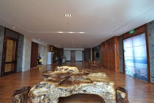 Un amplio vestíbulo de hotel con un gran mostrador de recepción de madera, una zona de estar y vistas al exterior a través de amplias ventanas.