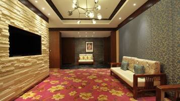 A hotel room with a red carpet, a sofa, a TV mounted on a textured wall, and a chandelier.