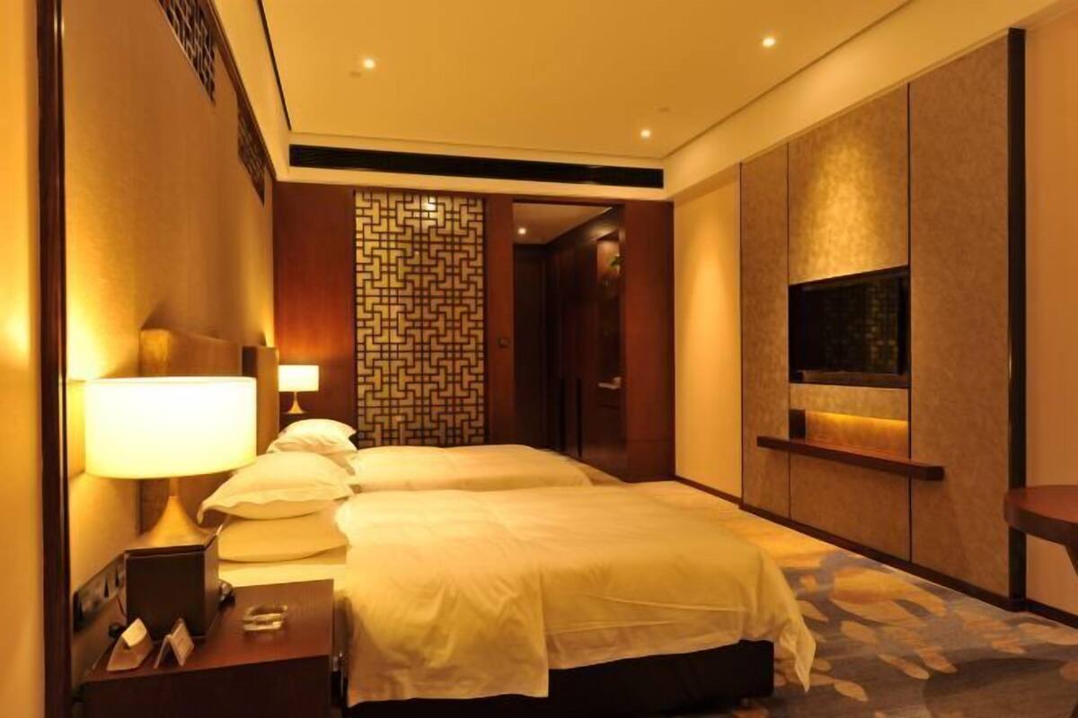 Een hotelkamer met twee bedden, een televisie, een nachtkastje en een decoratief wandpaneel.