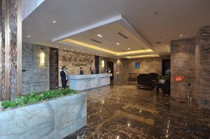 Un vestíbulo de hotel con una recepción, zona de estar y suelo de mármol.