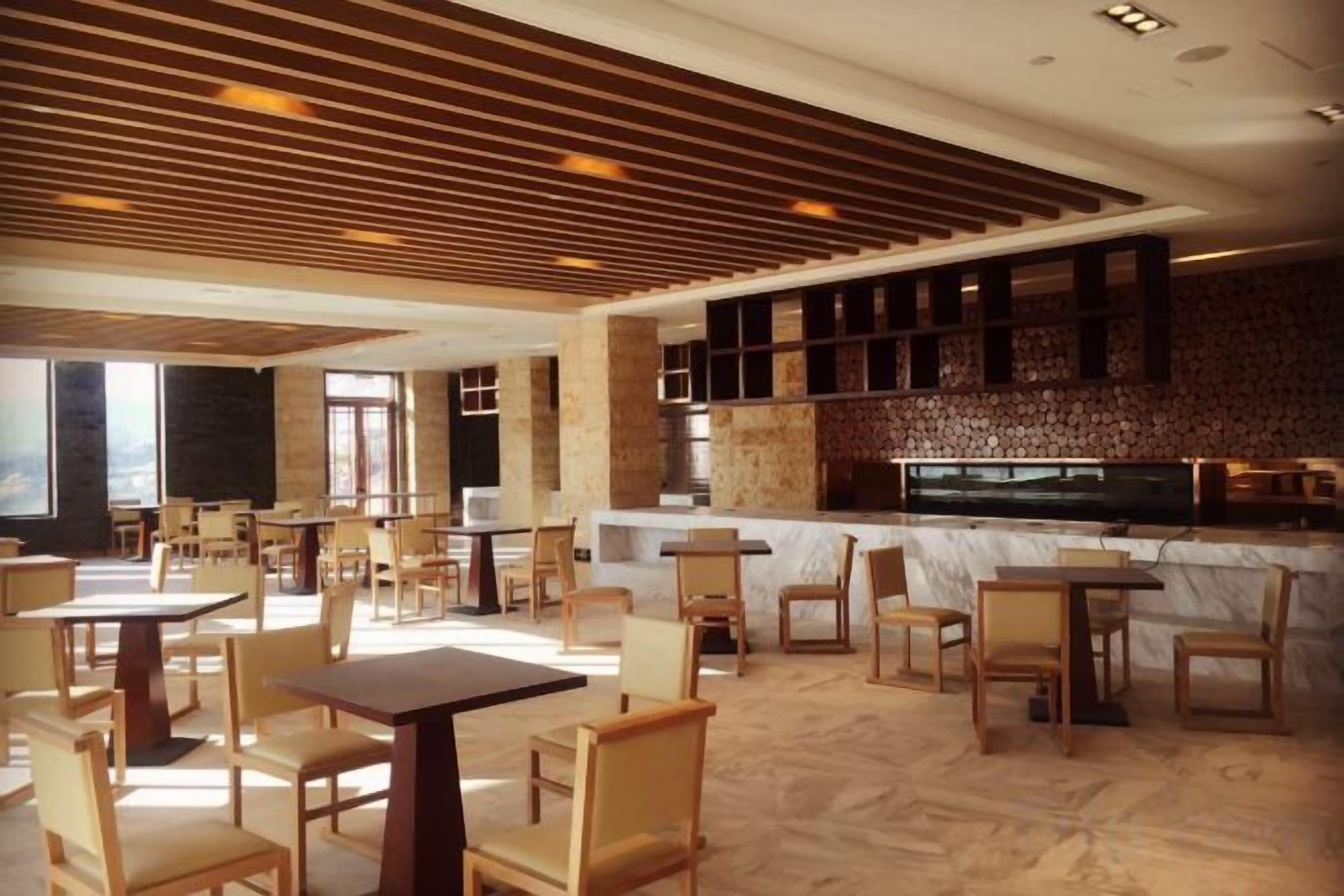 A modern restaurant with wooden tables and chairs, a marble counter, and a sloped ceiling with wooden panels.