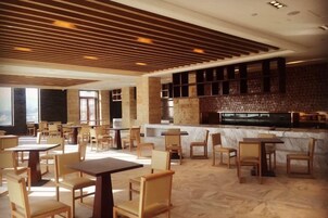Un restaurante moderno con mesas y sillas de madera, una barra de mármol y un techo inclinado con paneles de madera.