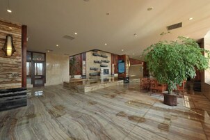 A spacious lobby with a marble floor, a large potted plant, and a reception desk.