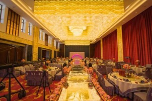 Un salón de banquetes con filas de mesas, un escenario y un telón rojo de fondo.