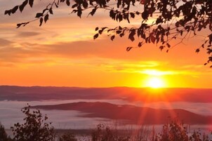Un atardecer sobre un paisaje montañoso, con vistas al sol ocultándose tras las colinas.