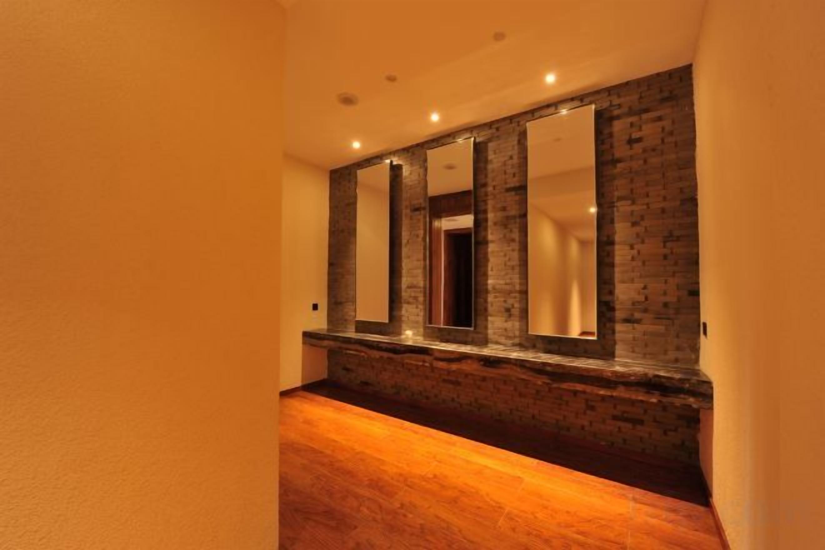Un pasillo con suelo de madera, pared de ladrillo y un espejo.