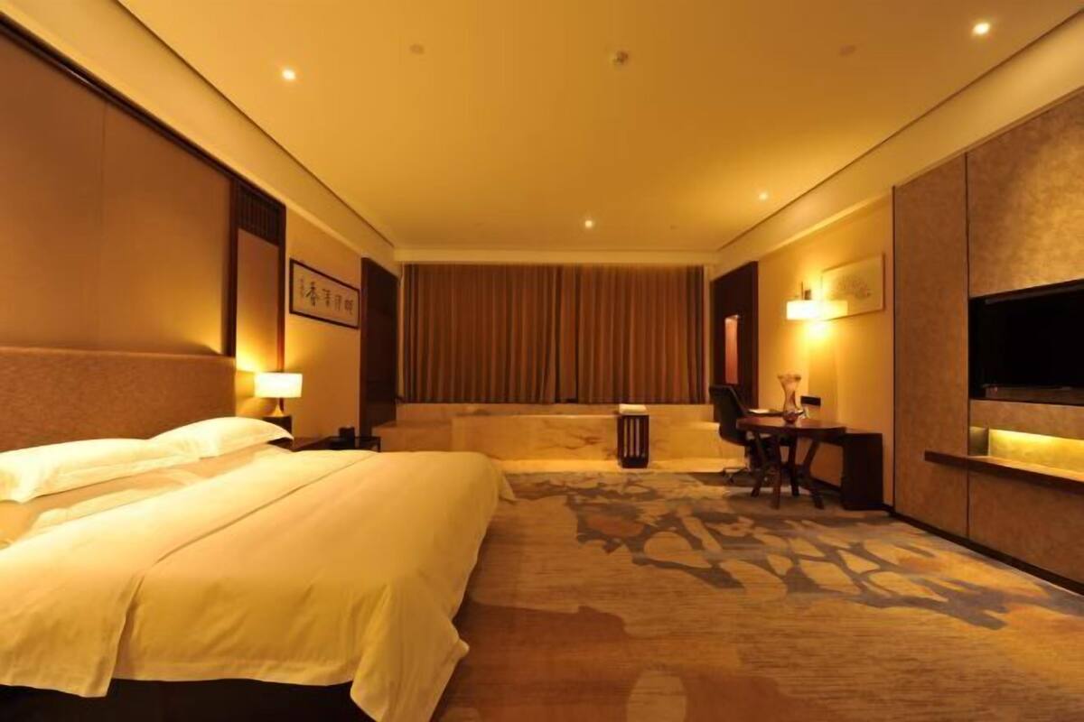 Een hotelkamer met een bed, een bureau, een stoel, een televisie en een gordijn.