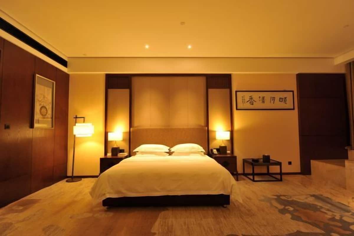Een hotelkamer met een groot bed, nachtlampjes, een klein tafeltje en een kunstwerk aan de muur.