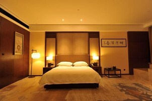 A hotel room with a large bed, bedside lamps, a small table, and a wall-mounted artwork.