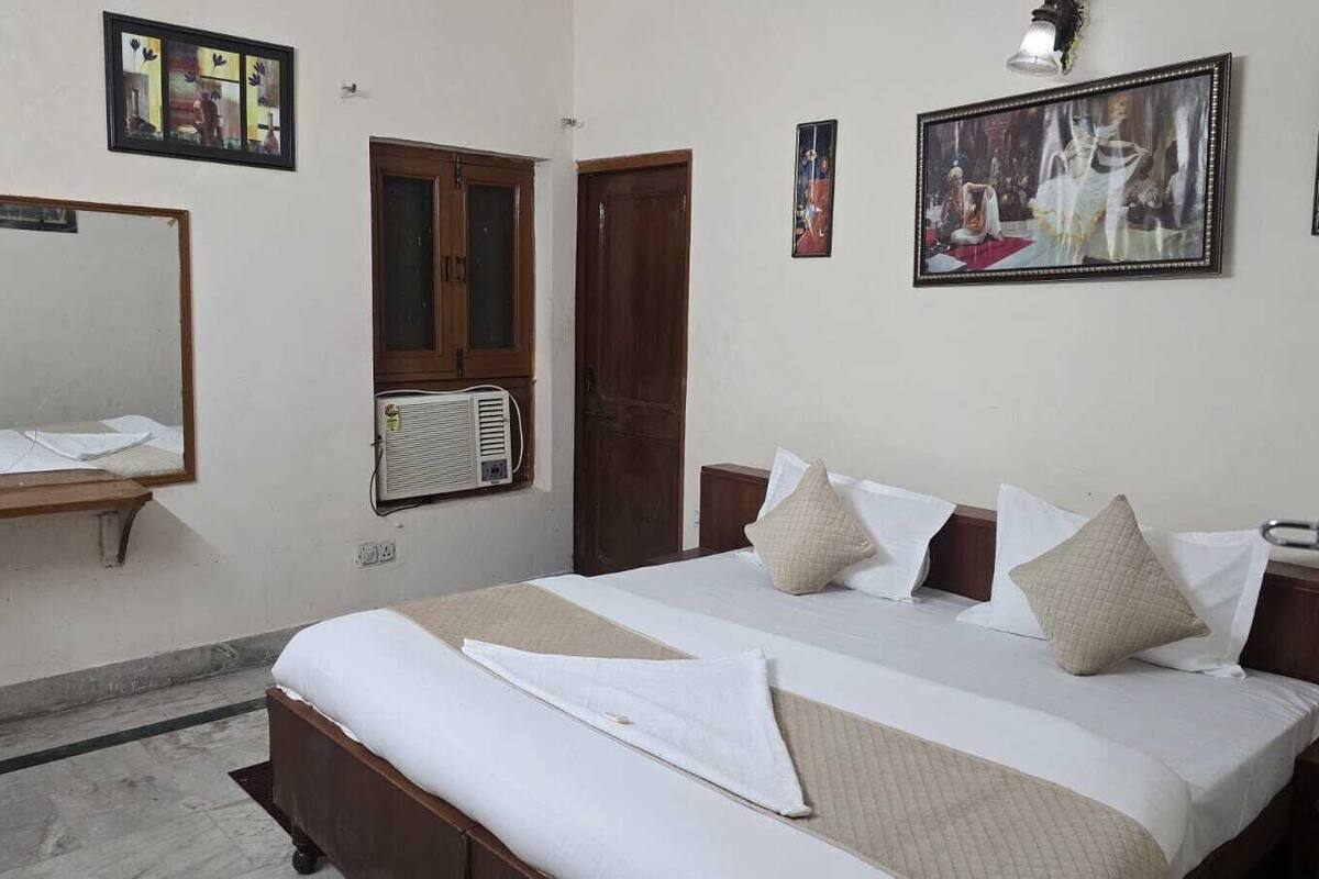 A hotel room with a large bed, a bedside table, a mirror, and a window with an air conditioning unit.