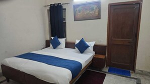A bedroom with a bed, two nightstands, a wooden door, and a wall-mounted painting. - Hotel maa heritage (Jaipur)