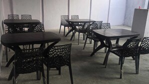 A series of tables and chairs arranged in a spacious indoor area with a concrete floor and white walls. - Hotel maa heritage (Jaipur)