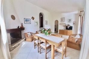 A living room with a fireplace, dining table, wicker furniture, and framed pictures on the walls. - <i>Reclaim your own space on Sardinia's south-eastern coast, in a secluded, sheltered home a stone's throw from the sea and the heart of Costa Rei.</i>Just steps from the <b>centre of Costa Rei</b> and only <b>300 metres from the white sandy beach</b>, < (Muravera)