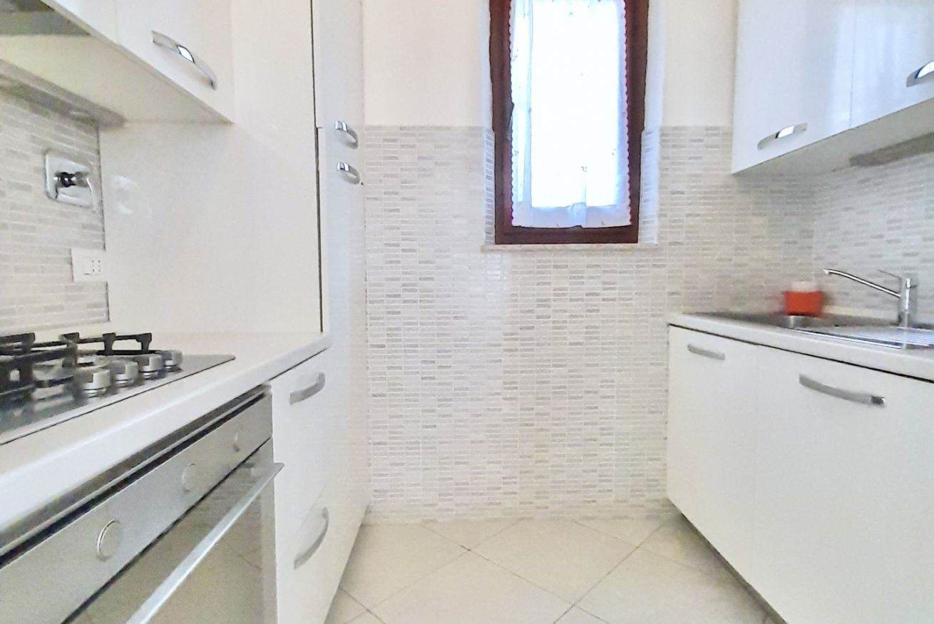 Una cocina con armarios blancos, una estufa a gas y un ventanal de marco marrón.