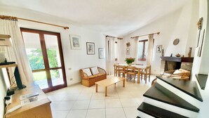 Ein geräumiges Wohnzimmer mit einem Holztisch, einer Couch und einem Essbereich mit Stühlen. Ein Kamin und eine Treppe in eine weitere Ebene sind ebenfalls vorhanden.