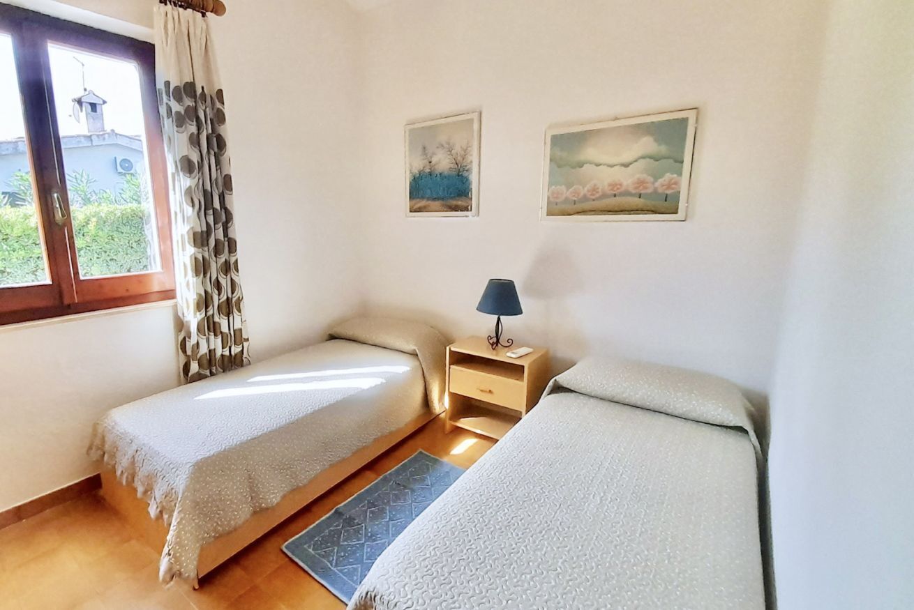 Ein Schlafzimmer mit zwei Einzelbetten, einem Nachttisch mit Lampe, einem Fenster mit Vorhängen und zwei Wandgemälden.