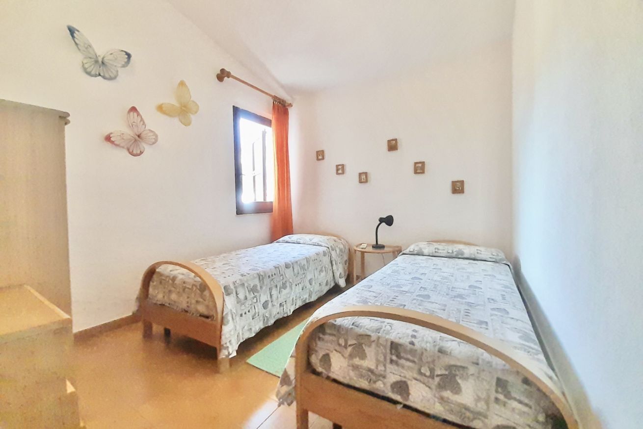 Quarto com duas camas de solteiro, janela com cortinas, uma mesinha e detalhes decorativos nas paredes, incluindo borboletas e pequenas imagens.