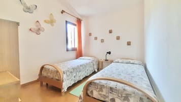 Quarto com duas camas de solteiro, janela com cortinas, uma mesinha e detalhes decorativos nas paredes, incluindo borboletas e pequenas imagens.