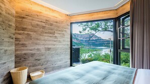 Un dormitorio con un ventanal que ofrece vistas a un paisaje montañoso y un lago.