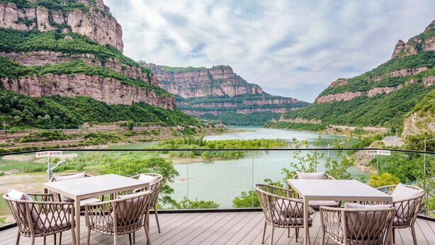 Una terraza con mesa y sillas, con vista a un río y montañas.