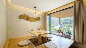 Una habitación moderna con una mesa de madera, asientos acolchados, un ventanal con vistas a zonas verdes y una original pieza de arte en la pared.