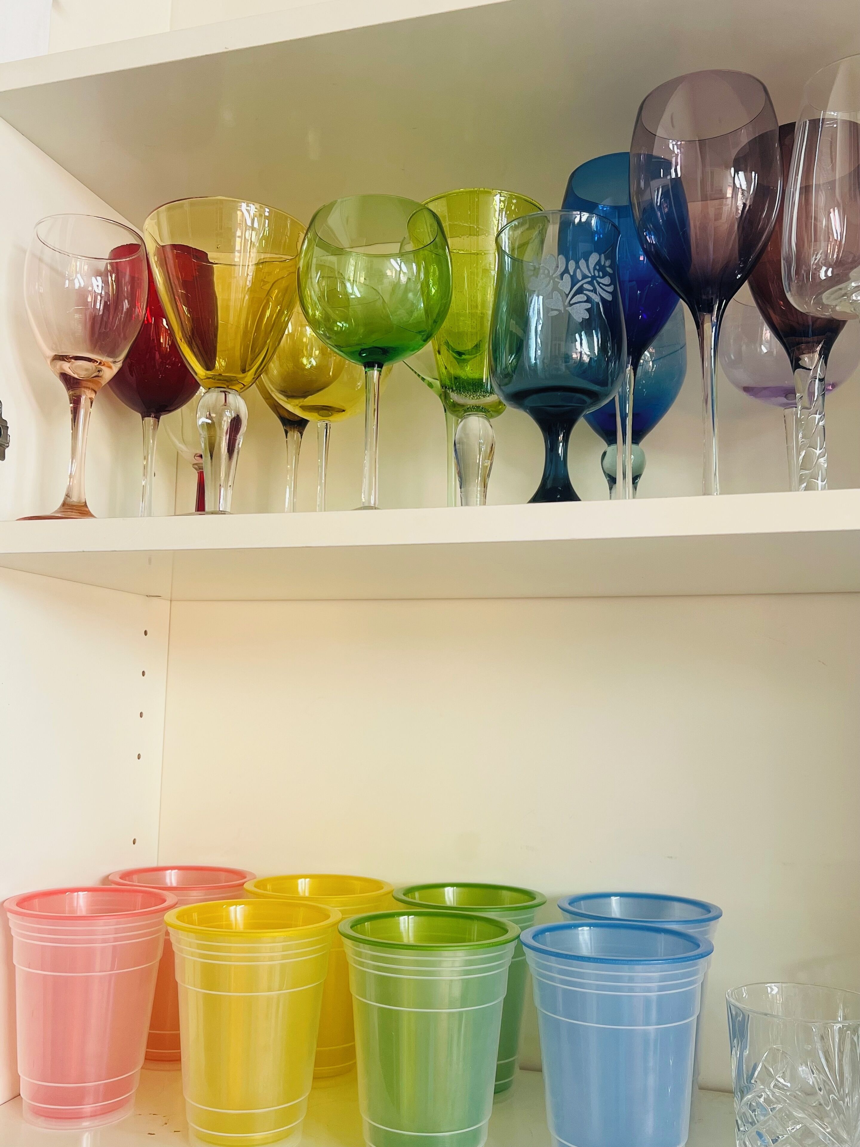 A shelf with various colored glassware, including wine glasses and plastic cups.