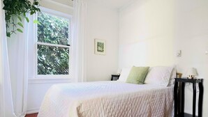 Un dormitorio con una cama grande, una ventana con cortinas, una mesita de noche y una planta colgante.