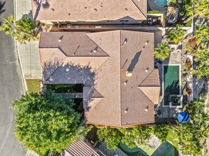 Luchtbeeld van een woonhuis met pannendak, een zwembad en omliggend groen.