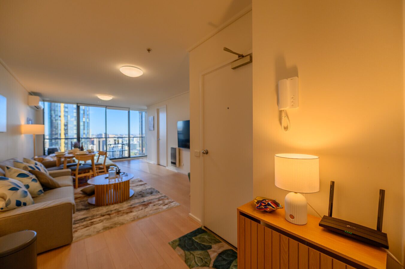 Un salon moderne avec un canapé, une table basse et un téléviseur. Il y a un balcon qui offre une vue sur les immeubles.