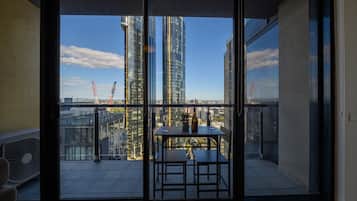 Un balcon avec une table et des chaises, un ventilateur, et une vue sur de hauts immeubles et des grues de chantier.