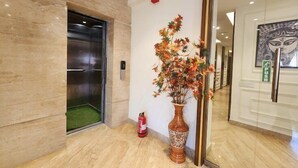 An elevator, a fire extinguisher, and a decorative vase with foliage. - EENNRA ARAMMBAGH (Arambag)