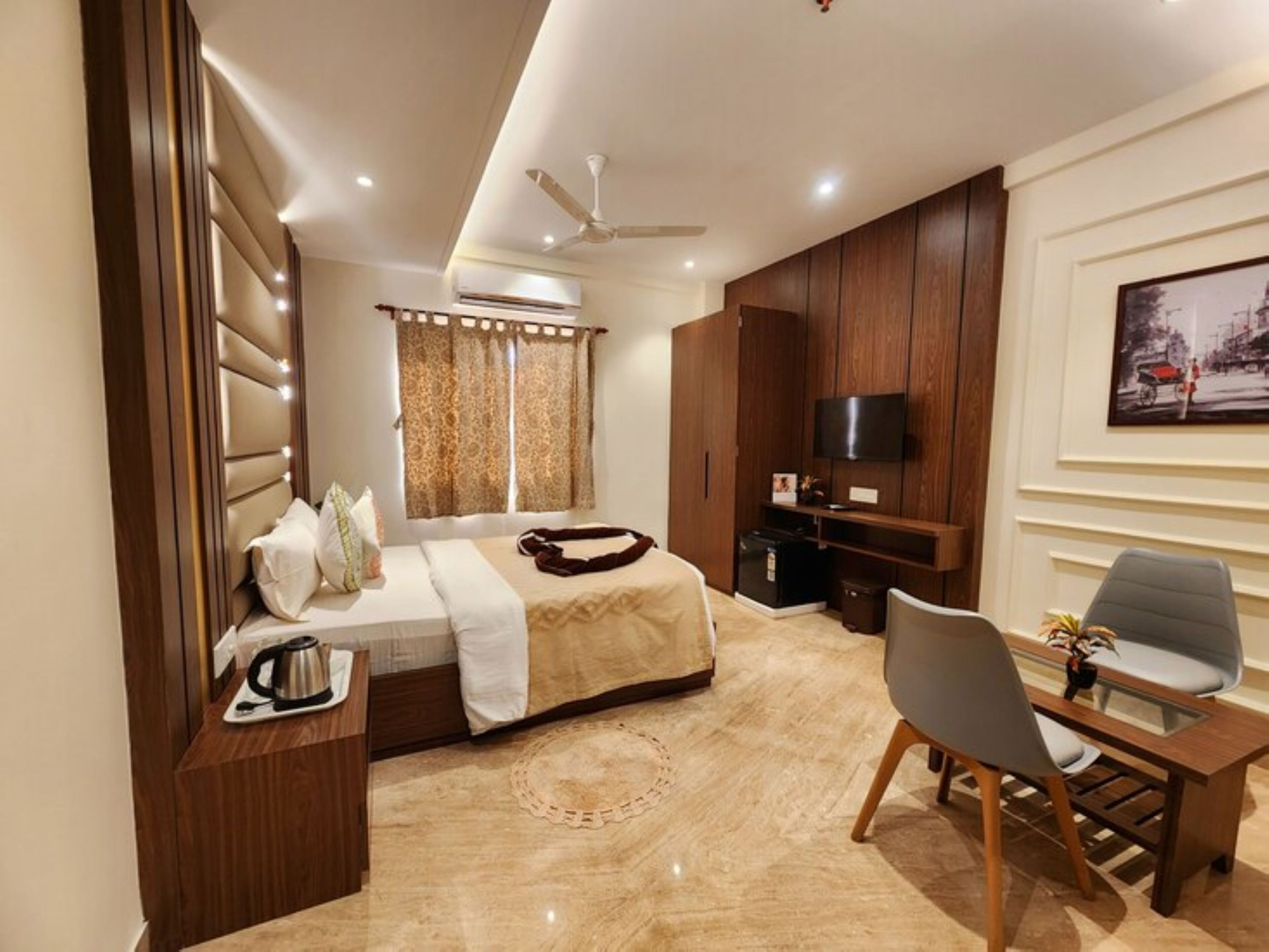 A modern hotel room with a bed, a desk, a chair, a TV, and a painting on the wall.
