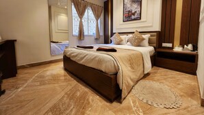 Une chambre à coucher avec un grand lit, une table de chevet, une commode, un ventilateur de plafond, une fenêtre avec des rideaux et un tableau encadré au mur.