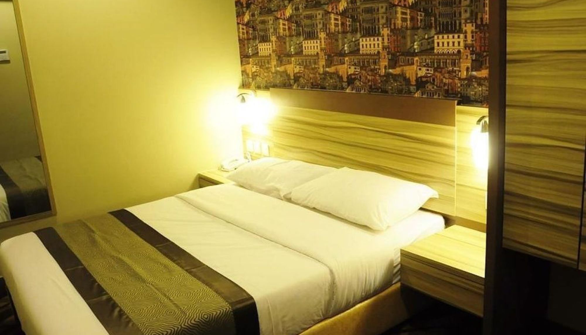 A hotel room with a bed, a nightstand, and a wall with a patterned mural.