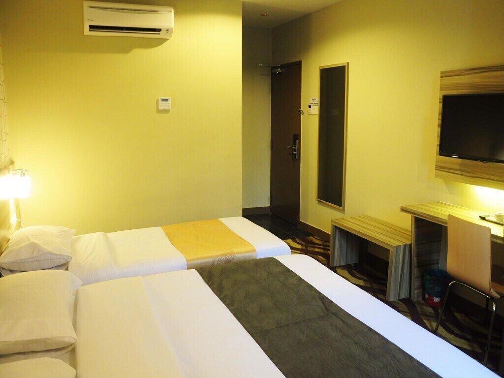 A hotel room with two beds, a desk, a chair, a TV, and an air conditioning unit.