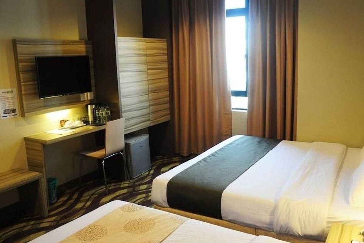Habitación de hotel con cama, escritorio, televisión y ventana con cortinas.