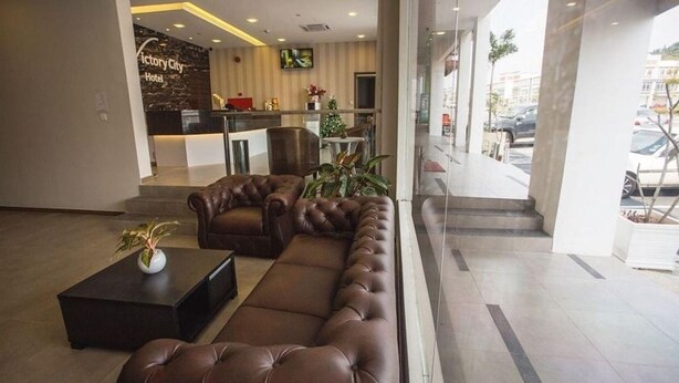 A hotel lobby with a reception desk, a seating area with a sofa and armchairs, and a potted plant. - Victory City Hotel Crystal Bay (Johor Bahru)