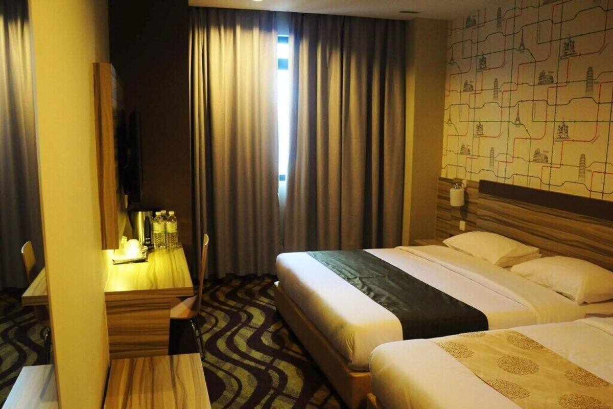 Habitación de hotel con dos camas, un escritorio con silla, televisor y ventana con cortinas.