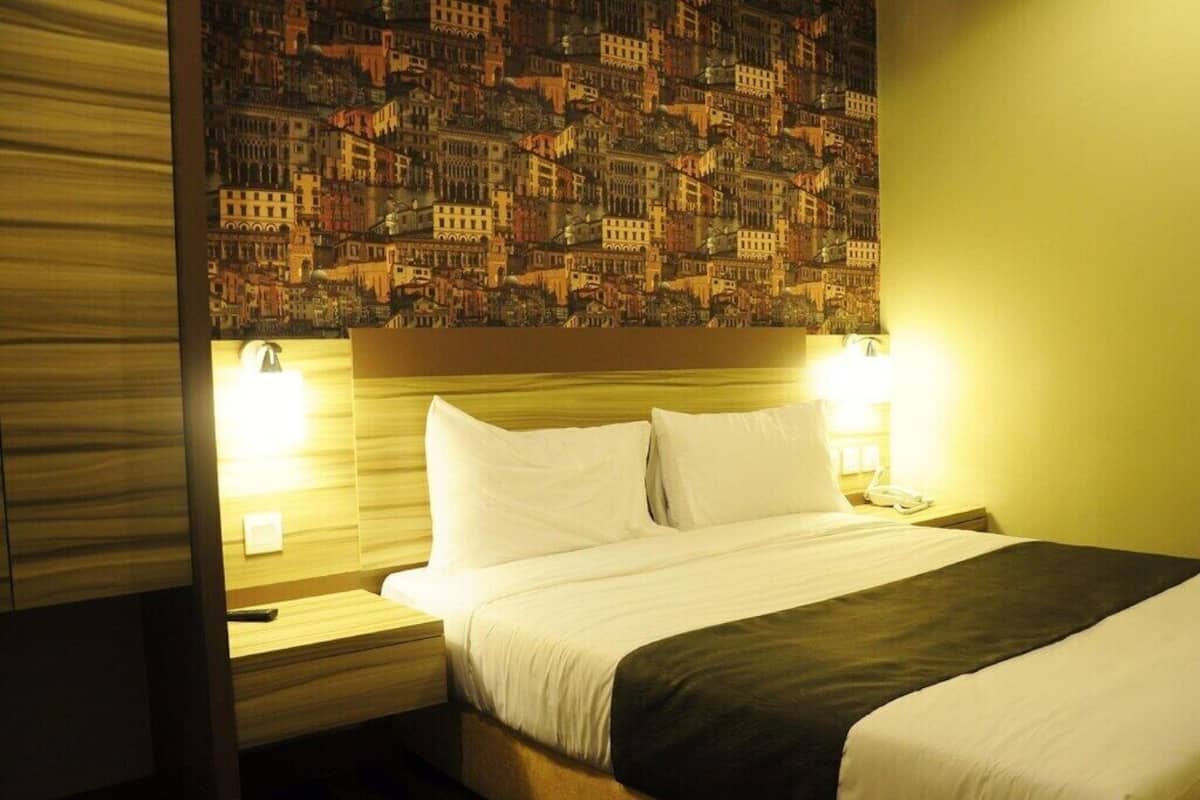 Habitación de hotel con cama, dos mesitas de noche y un cabecero con papel tapiz de paisaje urbano.