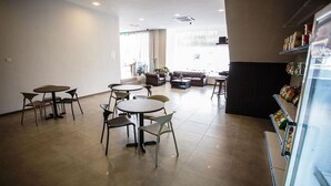A spacious indoor area with multiple round tables and chairs, a seating area with sofas, and a refrigerator stocked with beverages. - Victory City Hotel Crystal Bay (Johor Bahru)
