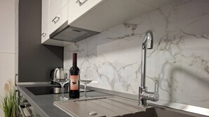 A modern kitchen with a marble backsplash, stainless steel appliances, and a wine bottle. - Apartments Tomislav (Vrsi)
