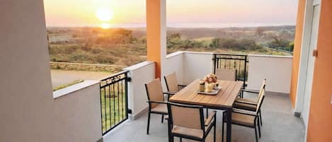 A balcony with a table and chairs, a view of the landscape, and a sunset.