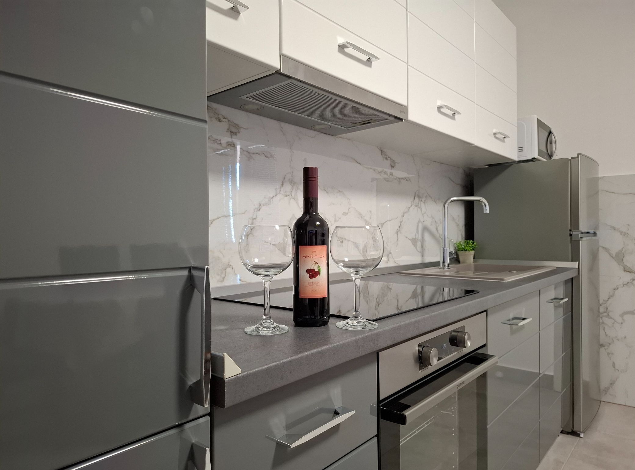 A modern kitchen with a wine bottle and two glasses on the counter, stainless steel appliances, and a marble backsplash.