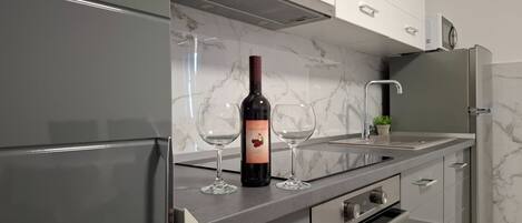 A modern kitchen with a wine bottle and two glasses on the counter, stainless steel appliances, and a marble backsplash.
