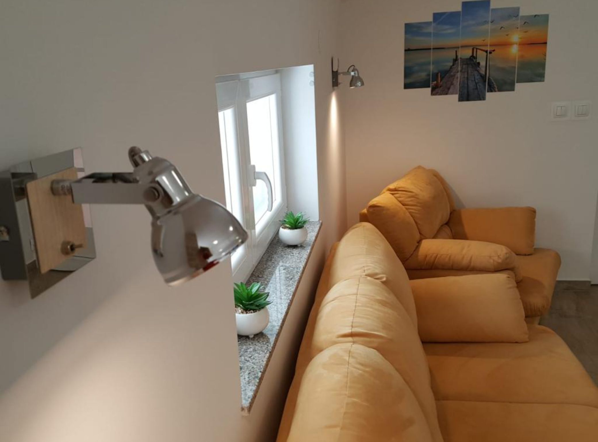 A modern living room with a sofa, a desk lamp, a window, and a wall-mounted mirror.