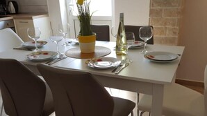 A dining table set with plates, cutlery, and wine glasses, with a vase of yellow flowers and a bottle of white wine. - Apartments Tomislav (Vrsi)