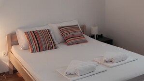 A neatly made bed with white linens, striped pillows, and rolled towels on a wooden headboard. - Apartment Ela (Sveti Filip i Jakov)