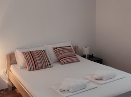 A neatly made bed with white linens, striped pillows, and rolled towels on a wooden headboard.